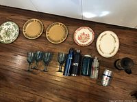 Four blue tinted plastic stemmed cups in front of water thermoses and cups, on wooden floor.