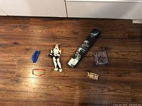 Photo of the lot items displayed on wooden floor: Stormtrooper Lego figure, Voldemort wand, mechanical speaker, wooden puzzle, wrist bracelet, finger scooter, and Naruto cube.