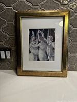 Front view of framed vintage print showing three women dancing, in gold frame and white mat.