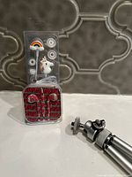 Colorful wired earbuds with rainbow and unicorn decorations and red wired earbuds in compact case, with small silver camera tripod mount visible