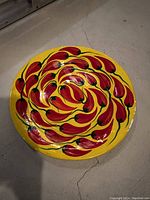 Top view of round ceramic plate showing vibrant yellow and red chili pepper spiral design.