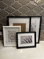 Four IKEA picture frames of varied sizes, two black and two white, arranged together against a patterned wall.