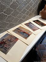 Five Picasso reprint prints laid out on a table with cream-colored mounts against a tiled wall backdrop. Each image depicts various Picasso-style figures in predominantly blue and rose color schemes.