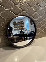 Round wall mirror placed against a tiled wall, showing clear reflection of kitchen interior, highlighting mirror's clarity and chrome frame.