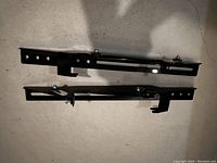 Black metal TV wall mount bracket shown flat with visible mounting holes and adjustment mechanism.