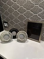 Front view showing three circular plaster photo frames (two off-white, one black) and one gold rectangular frame