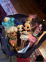 Bag with three Bratz dolls with distinctive colorful hairstyles and clothing, visible Barbie doll leg, and a pink bottle accessory.