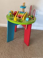 Full view of the baby activity table showing colorful painted wooden legs and top with various activity features including a xylophone and bead maze.