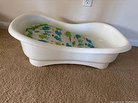 Side view of white plastic baby bathtub with colorful animal print foam mat inside