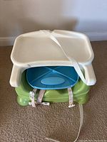 Image showing white detachable eating tray strapped on top of green base booster seat with a blue segmented tray inside.