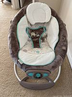 Front angle view of the baby bouncer showing plush cushioning, animal print fabric, and control panel at base.