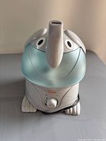 Front view of the Crane baby elephant humidifier showing the dial control, elephant face, ears, and trunk with power cord wrapped at the base.