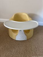 Yellow Bumbo infant seat with white plastic tray attached, showing front view and branding.
