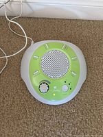 My Baby Sound Machine on carpet with power cord plugged in. Green control panel with speaker grill and knobs visible.