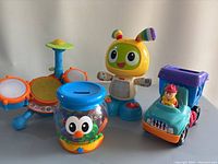 Photo showing four Fisher Price toys: interactive robot, drum set, toy truck, and owl jar toy.