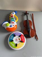 Top view of the colorful electronic saxophone toy, the small violin with bow, and the round electronic music toy with instrument icons.