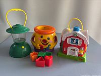 Photo showing the three baby toys together: green lantern, dog-shaped toy, and toy barn with shape blocks