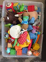 Overhead view of plastic bin filled with various baby toys including plush animals, blocks, and fabric books.
