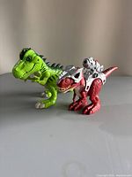 Photo showing green Tyrannosaurus Rex and red robotic mechanical dinosaur toys from front angle.