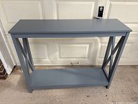 Full front view of the grey entrance table showing rectangular top, bottom shelf and cross support sides.