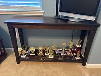 Front view of the dark brown wooden entrance table with trophies underneath on the floor, trophies not included.