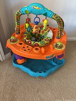 Front angle of Evenflo Exersaucer SmartSteps showing colorful arch with hanging toys and padded seat.