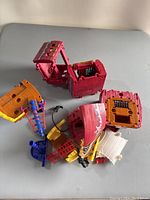 Various plastic parts of a Fisher Price Imaginext Pirate Ship including large red hull sections, yellow and orange deck pieces, blue and red ladders, and a black anchor accessory, laid out unassembled on a surface.