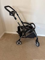 Side view of Graco SnugRider Elite stroller frame showing frame, wheels, and handlebar.