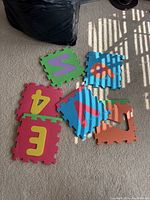 Several colorful foam mat pieces with letters including A, E, V, W, and an animal figure piece lying on carpeted floor.