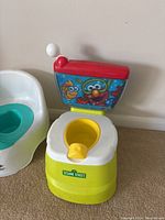 Sesame Street Elmo potty chair with colorful backrest, yellow potty bowl, red lid with pull handle, placed on carpeted floor against white wall