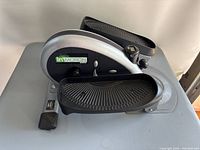 Front-angle view showing the side of the stepper with green InMotion branding, black textured foot pedals, and resistance knob.