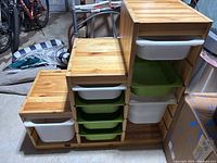 Photo showing wooden storage shelf with plastic bins in white and green, three tiers with various bins inserted.