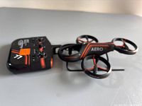 Photo showing the Sharper Image X-Treme Aero mini drone with its black and orange color scheme, four propellers with circular guards, and the Aero branding.