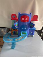Front view of PJ Masks Deluxe Battle HQ playset showing ramps with character stickers and multi-level structure with two red doors on top.