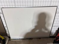 Full view of white dry erase board leaning against a wall with grid measurement background, showing its size and frame.