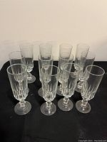 12 clear ribbed glass champagne flutes arranged on a black surface, showing the front view of the flutes.