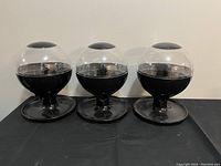 Photo shows 3 black and clear automatic candy dispenser machines side by side on a black surface.