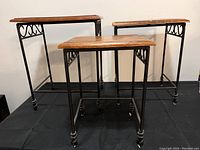 Three nesting tables with wood tops and wrought iron legs arranged side by side