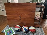Closed arcade basketball cabinet with three basketballs and instruction manual positioned in front on a cloth.