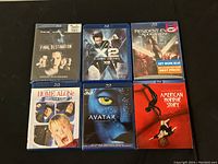 Photo showing six assorted Blu-ray cases arranged in two rows of three on a dark surface, titles clearly visible.