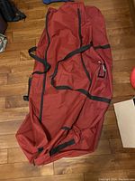 Red Christmas tree storage bag with black straps on wooden floor.