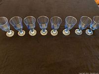 Eight cobalt blue water goblets lined up on a dark surface, showing ribbed detail and bases.