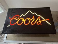 Front view of the black Coors Light sign illuminated showing red Coors script and white mountain outline.