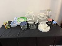 Photo showing various glass and plastic food storage containers, silicone lids, and glass jars with lids arranged on a table.