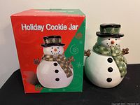 Photo of the snowman cookie jar next to its original colorful box labeled 'Holiday Cookie Jar' showing the jar and box in full view.