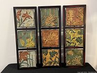Front view of three vertical metal wall art panels, each containing three textured square panels with raised floral and leaf designs, framed in black metal.