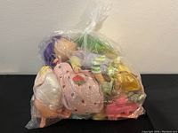 Plastic bag containing vintage Strawberry Shortcake dolls with different hair colors, dresses, and small pet figures inside the bag.