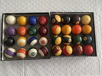 Two sets of pool balls in boxes, one modern, one vintage, showing all balls numbered and arranged in 4x5 grids.