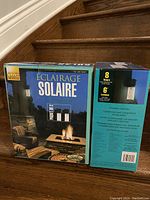 Two boxes of solar powered outdoor lights showing front and sides, both sealed and new.