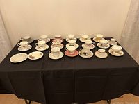 Full set of 18 tea cups each with matching saucer plus two extra saucers, displayed on black cloth surface.